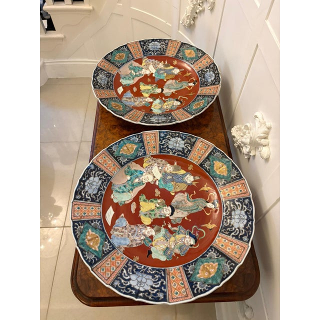 A striking pair of large Japanese Imari porcelain chargers, beautifully decorated with a lively scene depicting the...