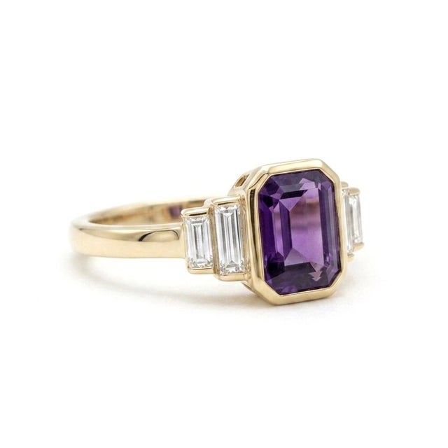 Refined and architectural, this stunning ring features a vibrant 7x5mm emerald-cut amethyst, secured in a sleek,...