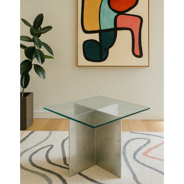 Mid Century Modern side table featuring an intersecting chrome base topped with a thick, green-edge glass surface....