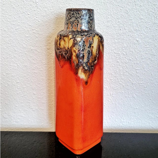 A tall, rectangular, persimmon-orange vase from Ü-Keramik that transitions at the shoulder to a round neck and mouth...
