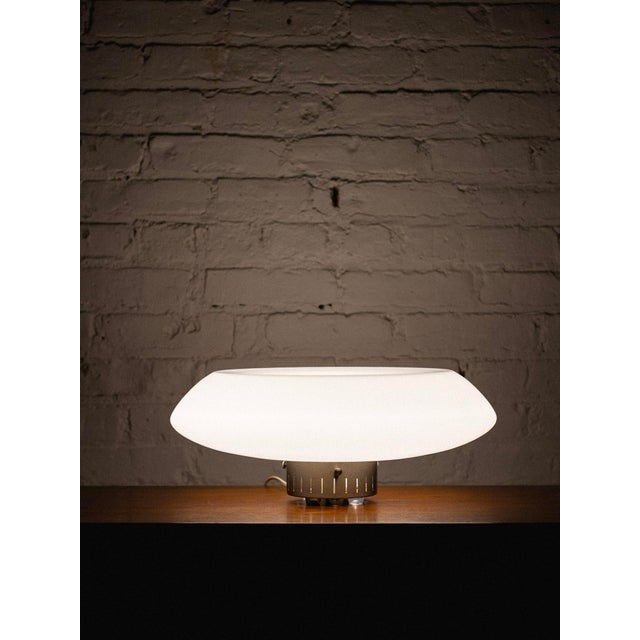 Table lamp with space-age, saucer-like design. The white glass top provides soft, but far-reaching light diffusion, while...
