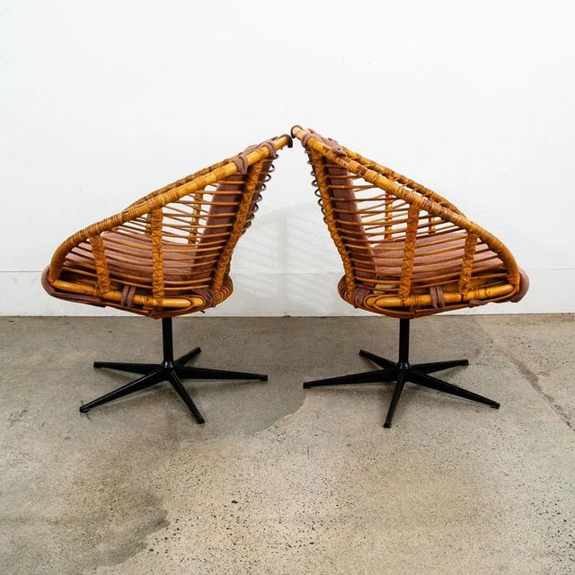 This is a pair of rattan swivel lounge chairs with pink / rose fabric cushions. The chair frames sit on black swivel...