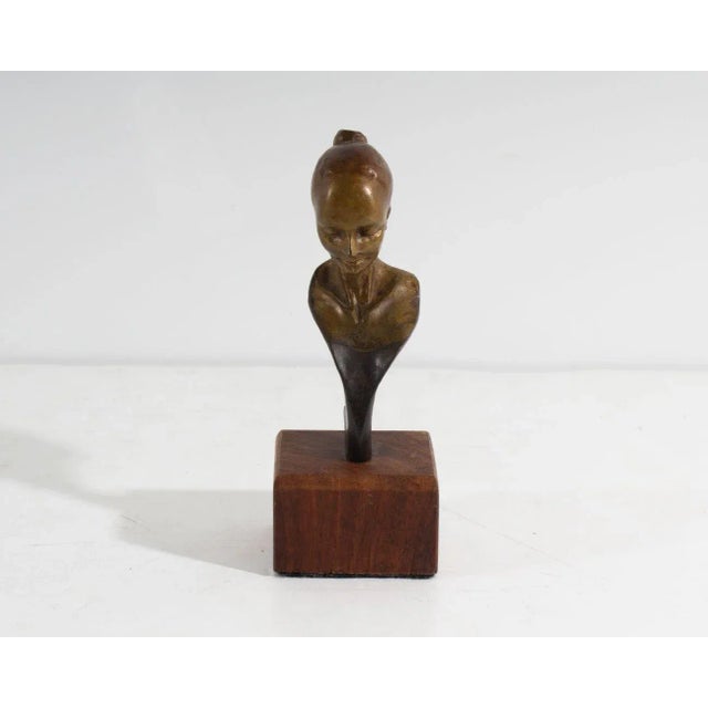 A signed miniature bronze sculpture. Signed to the back, the sculpture depicts the bust of a woman with her hair pulled...