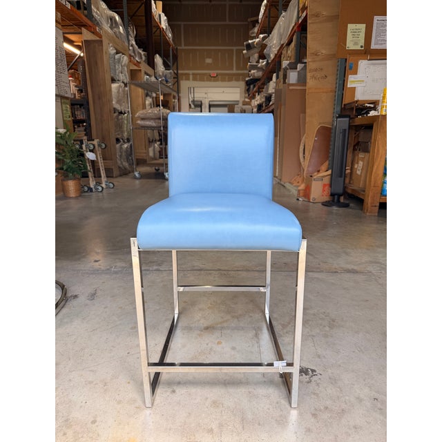 Contemporary counter stool featuring smooth sky blue genuine leather upholstery paired with a sleek stainless steel sled...