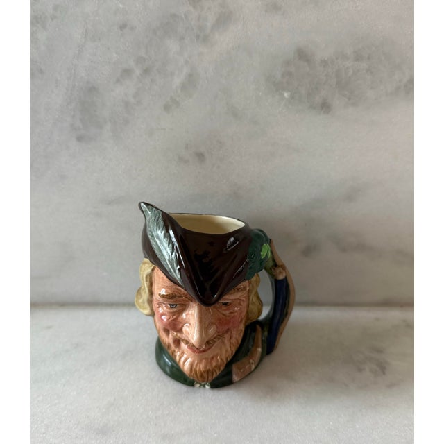 Vintage Royal Doulton small 4" hand painted mug of Robin Hood wearing a green tuinc and brown hat. Manufactured in 1959...