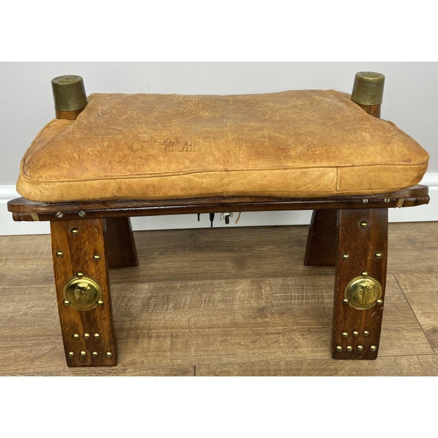 A distinctive Vintage leather footstool , combining rustic charm with striking decorative brass elements and a beautifully...