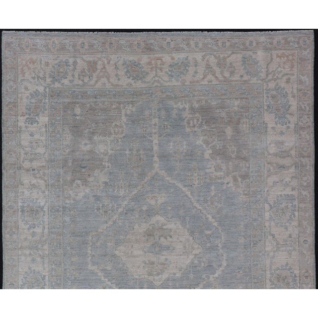 Measures: 5'10 x 8'9 Modern Oushak with a Light Blue-Gray Background with Medallion & Tribal Motifs. Country of Origin:...
