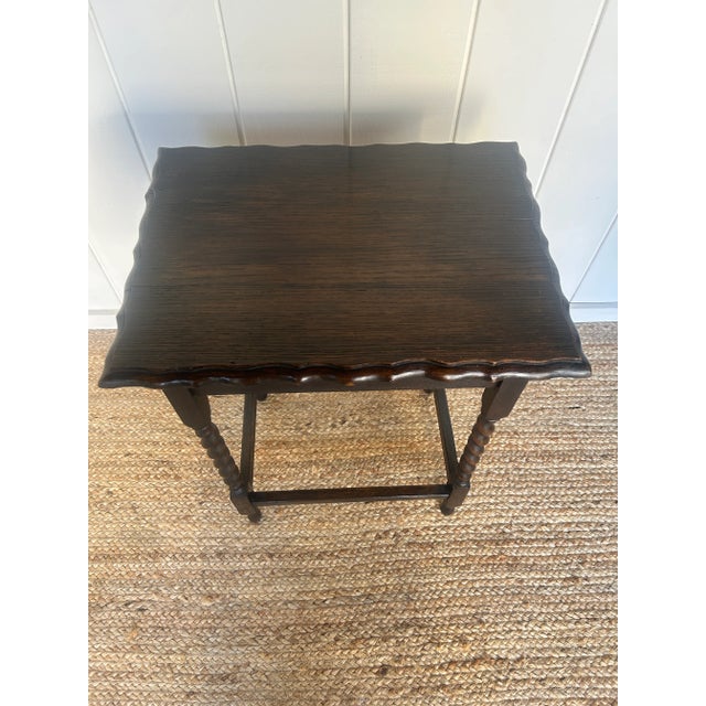 An antique English side table with beautifully turned barely twist legs and a scalloped edge top. Crafted from dark...