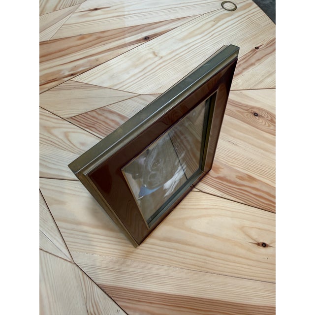 A tabletop picture frame with a glossy burgundy border and slim brass-tone trim around the outer edge and photo opening....