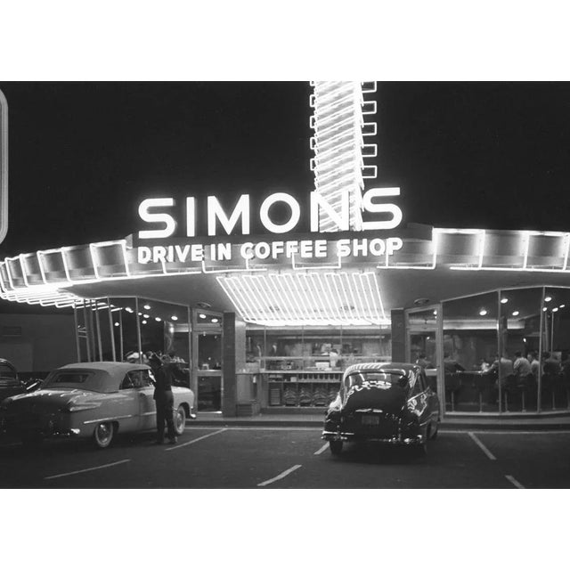The neon lights illuminate the night sky in this black and white monochrome print of the Simons drive-in coffee shop, a...