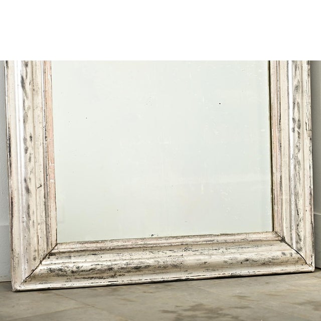A French 19th century Louis Philippe mirror with an understated, silver gilt frame enhanced by dark oxidation and...