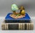 Fascinating, diminutive diorama featuring colorful mushrooms and a frog. The base is depicted as a wood grain and the...