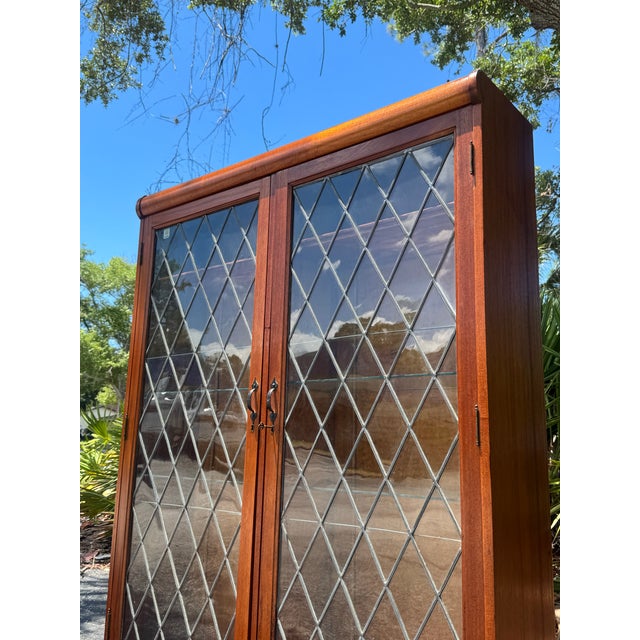 A beautiful vintage illuminated curio cabinet featuring elegant diamond pane glass doors, rich warm wood tones, and built-...