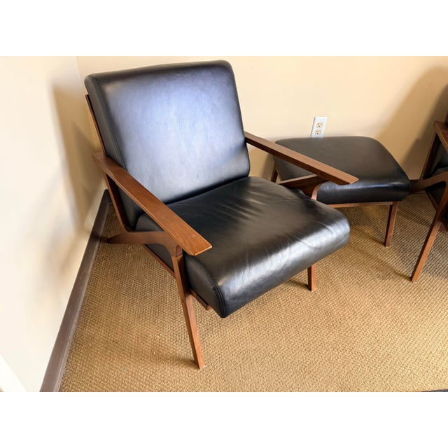 A handsome pair of mid-century style lounge chairs with matching ottoman, featuring sleek black leather upholstery and...