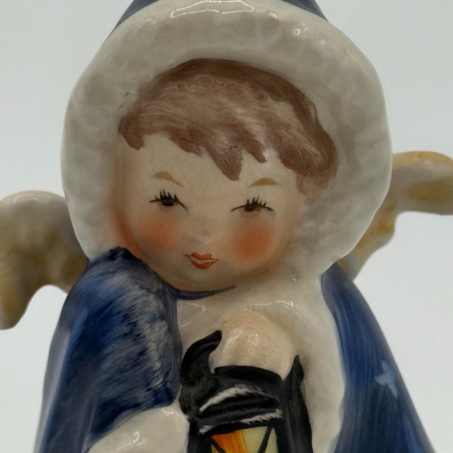 Add this charming Goebel West Germany porcelain angel dressed in a deep blue winter coat and holding a lantern, with sweet...