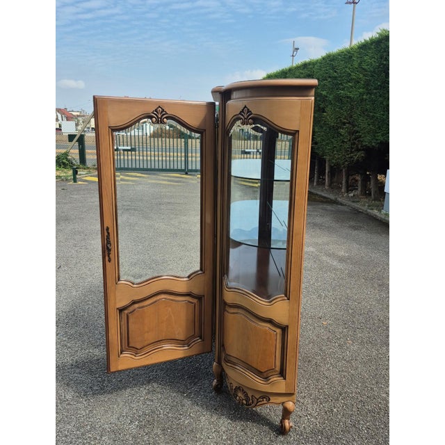 An elegant French Louis XV style cherrywood display cabinet dating from the 20th century. It features a curved glass front...