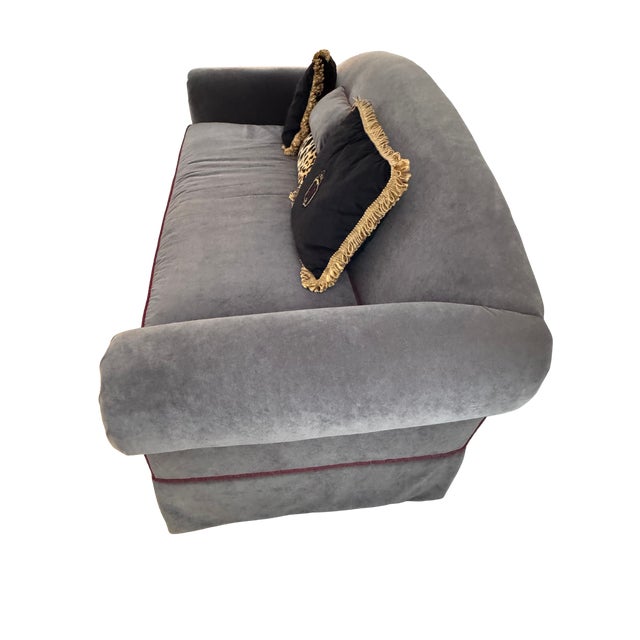 Camelback sofa in gray velvet, designed with a single bench cushion, a skirted base, and accented with contrasting red...