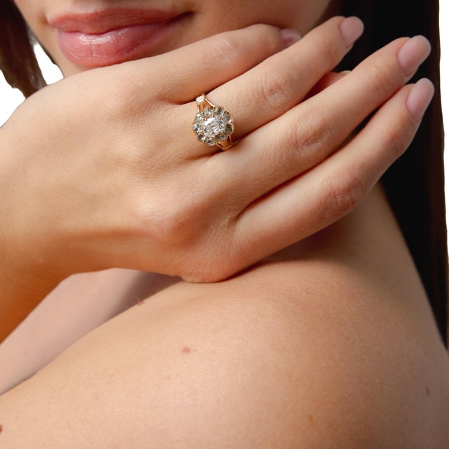 This charming antique cluster ring showcases a beautifully balanced 1.00 carat old mine cut diamond, glowing with soft,...