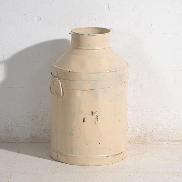 This set of two antique painted tin milk cans features two cylindrical containers with a narrowed upper neck, side handles...