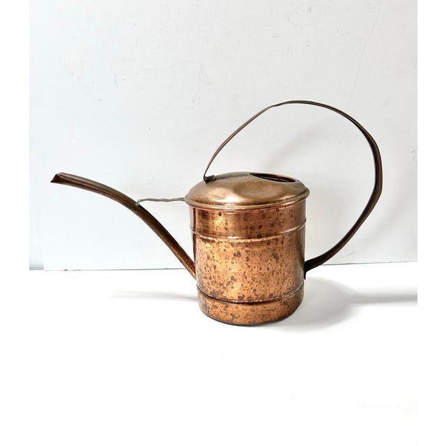 A beautifully aged vintage copper watering can featuring a long swan-neck spout and sculptural curved handle. The warm...