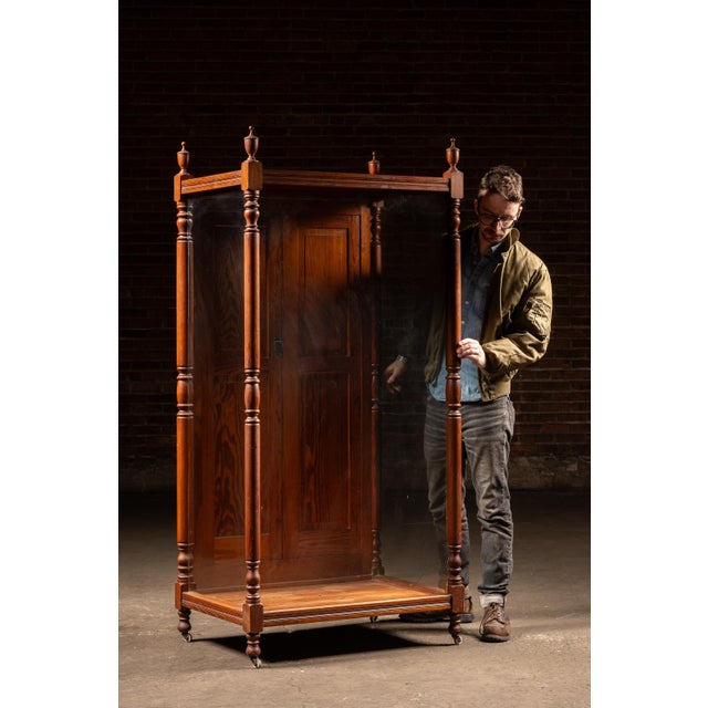 Tall oak retail display cabinet featuring paneled double doors and large glass viewing panels on three sides, framed by...