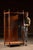 Tall oak retail display cabinet featuring paneled double doors and large glass viewing panels on three sides, framed by...