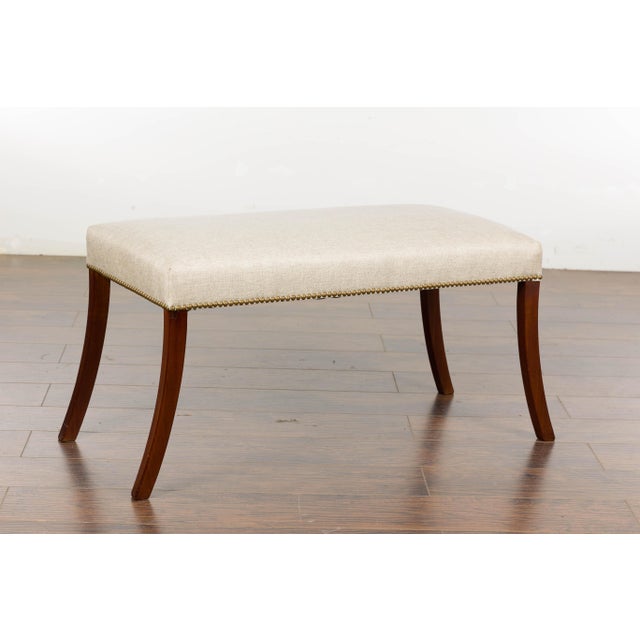 An English Regency bench from the 19th century with four saber legs and new custom linen upholstery with brass nailhead...