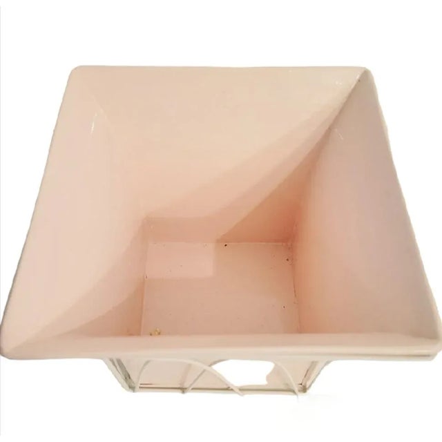 A pretty pale pink lacquered metal caged planter pot. The pot is made of metal and has been lacquered in a pale pink color...