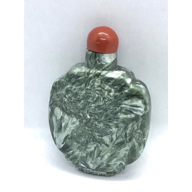 The elegant snuff bottle is made of Seraphinite, a green stone that is laced with shimmering patterns of silver. When it...