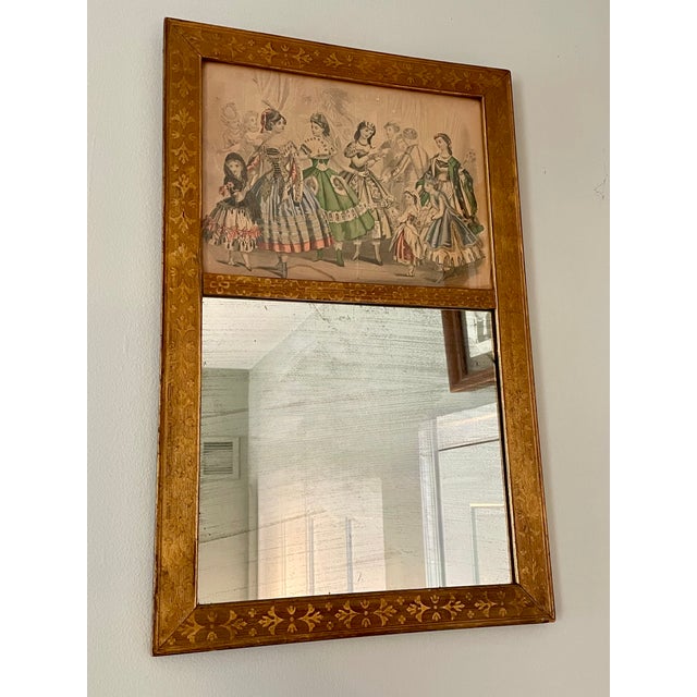 A small gilt wall mirror w/ a hand-colored fashion plate in the upper register. The frame is finely patterned with...