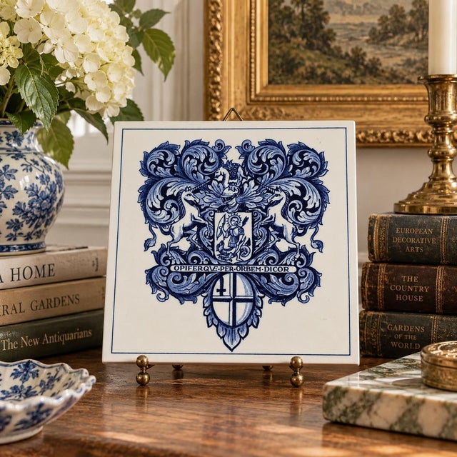 A classic Dutch Delft-style hand painted blue and white porcelain tile featuring an intricately rendered heraldic coat of...
