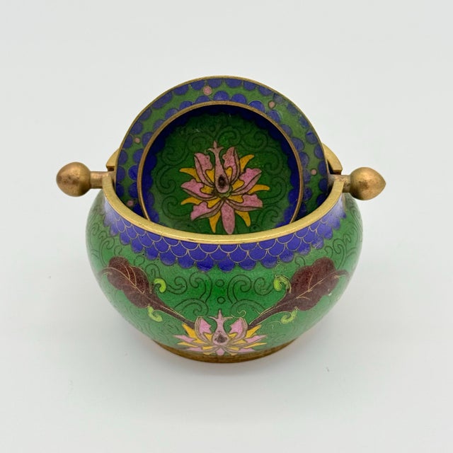 A jewel-like mid-century cloisonné ashtray with an unexpectedly clever bit of engineering. The rounded green enamel body...