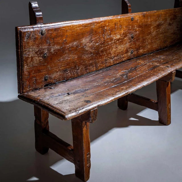 Long bench made of solid wood with a beautiful patina and iron rivets. The bench stands on three legs, with the backrest...