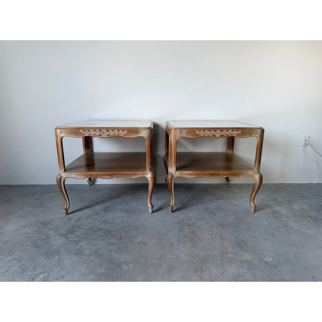 Beautiful pair of vintage French Provincial end tables featuring elegant marble tops, carved floral apron details,...
