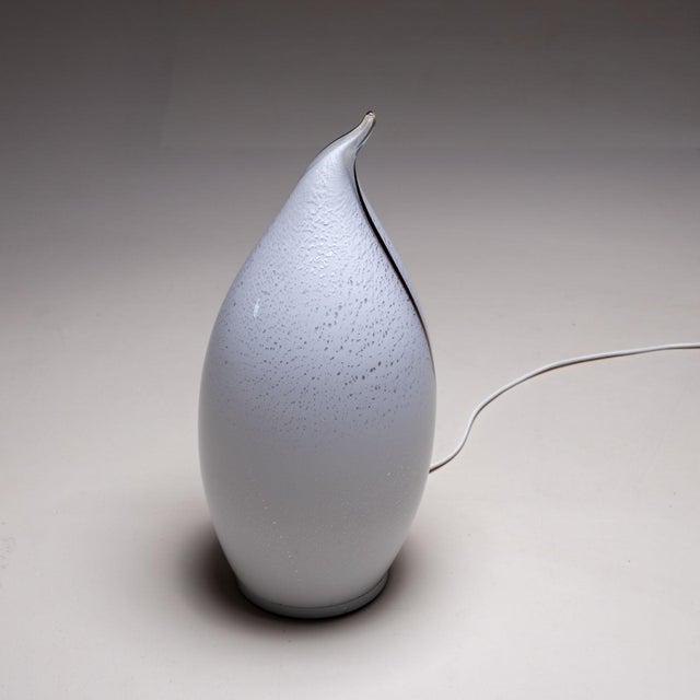 Small Murano glass table lamp with a white, drop-shaped body with air bubble inclusions and a black line.