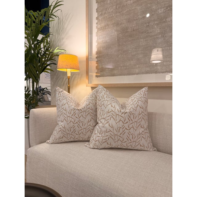 This decorative pillow features a soft ivory and cream background accented with a delicate warm beige botanical branch and...