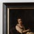 Early 19th-century original oil on canvas painting depicting a seated young woman illuminated by soft window light. In her...