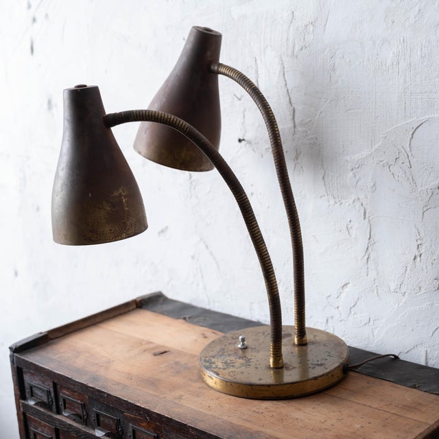 Compact twin-light desk lamp with patinated brass base and two independently adjustable gooseneck arms terminating in...