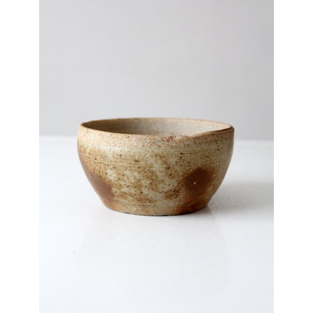 A vintage studio pottery bowl in an organic modern style, finished in a soft tan glaze with warm brown accents that drift...