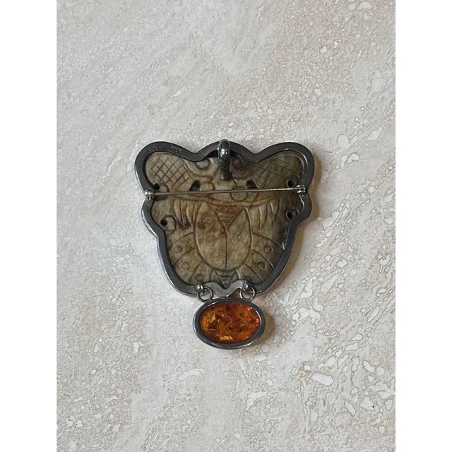This vintage brooch centers on a substantial carved stone plaque, its irregular, scalloped silhouette shaped with flowing...