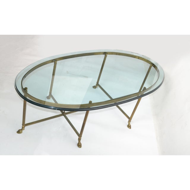 Hollywood Regency Mastercraft brass coffee table with hoof feed & thick classical racetrack glass top. The base shows a...