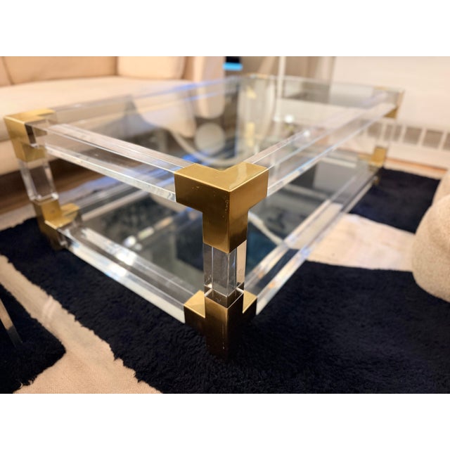 Jonathan Adler Jacques Grand Cocktail Table in clear acrylic, brushed brass and glass. One of Jonathan Adler’s signature...