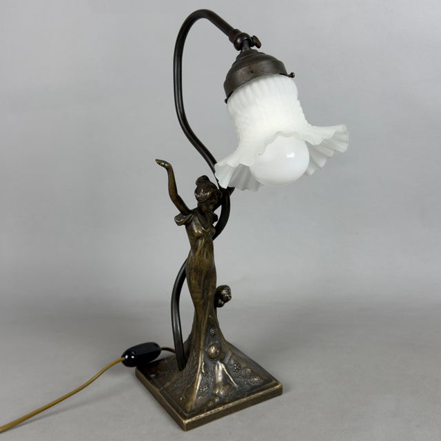 A dramatic and elegant Art Nouveau-inspired table lamp, in which the sculptural plasticity of metal blends with the grace...