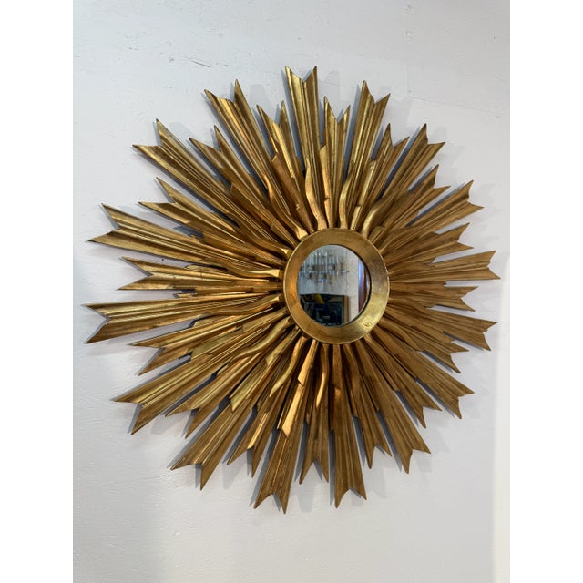 This striking wall mirror features an elaborate sunburst design, with a circular central mirror surrounded by an array of...