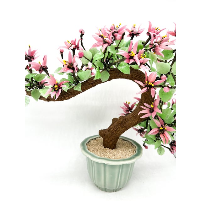 A striking oversized handcrafted glass bonsai tree featuring delicate pink jade-like blossoms, translucent green leaves,...