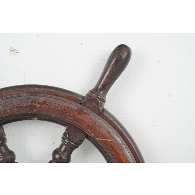 Vintage wood ship wheel with six spokes and a heavy brass center hub. It is characteristic of smaller maritime vessels or...