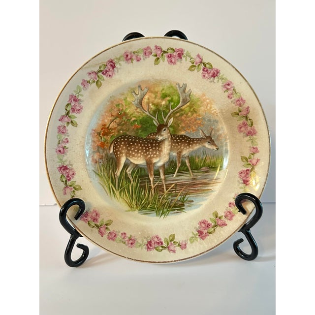 Antique transferware plate with a deer couple in a wooded setting. The woodland scene is surrounded by pink roses and gold...