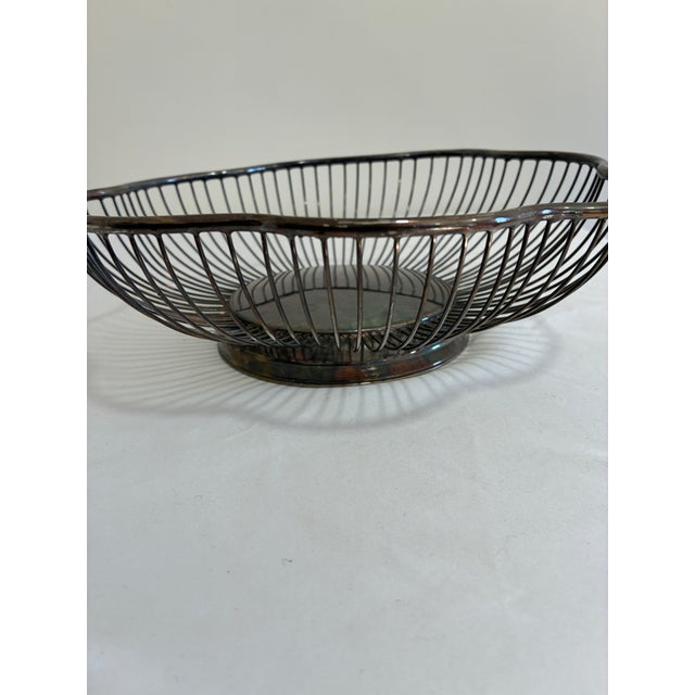 A vintage silverplate wire basket featuring a sculptural scalloped rim reminiscent of flower petals. Its radiating wire...