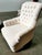 Armchairs with wooden frames and white fabric upholstery, button tufting on the back and arms, and studs on the bottom....