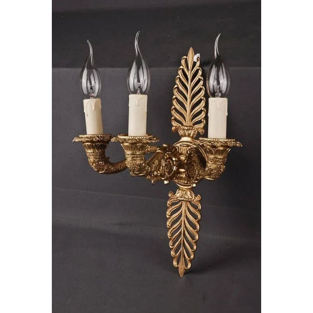 Decorative wall light in Empire style. Finely engraved and cast bronze. Three stylized, full horn-formed, sweeping light...